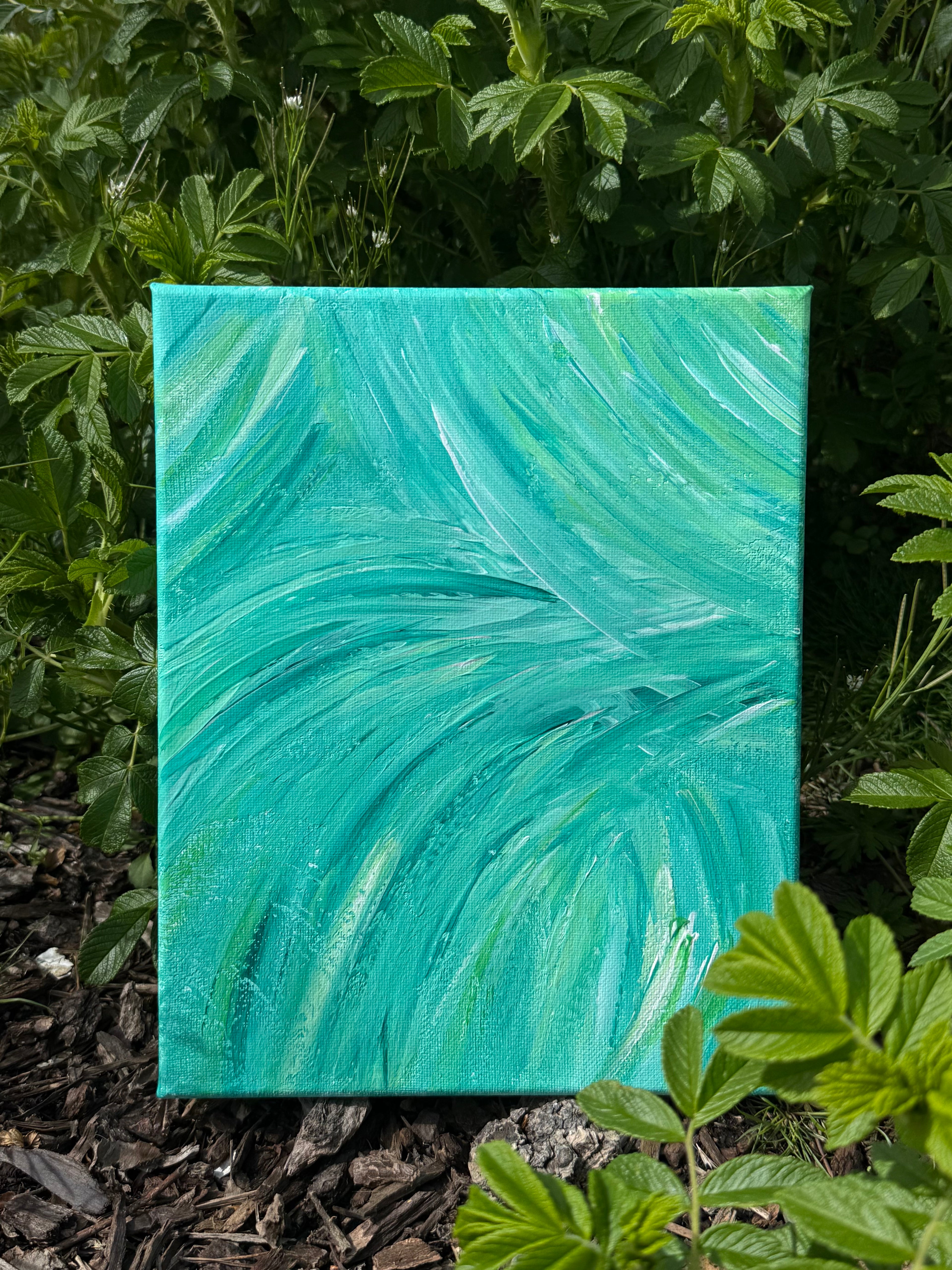 Turquoise abstract painting on canvas surrounded by green foliage