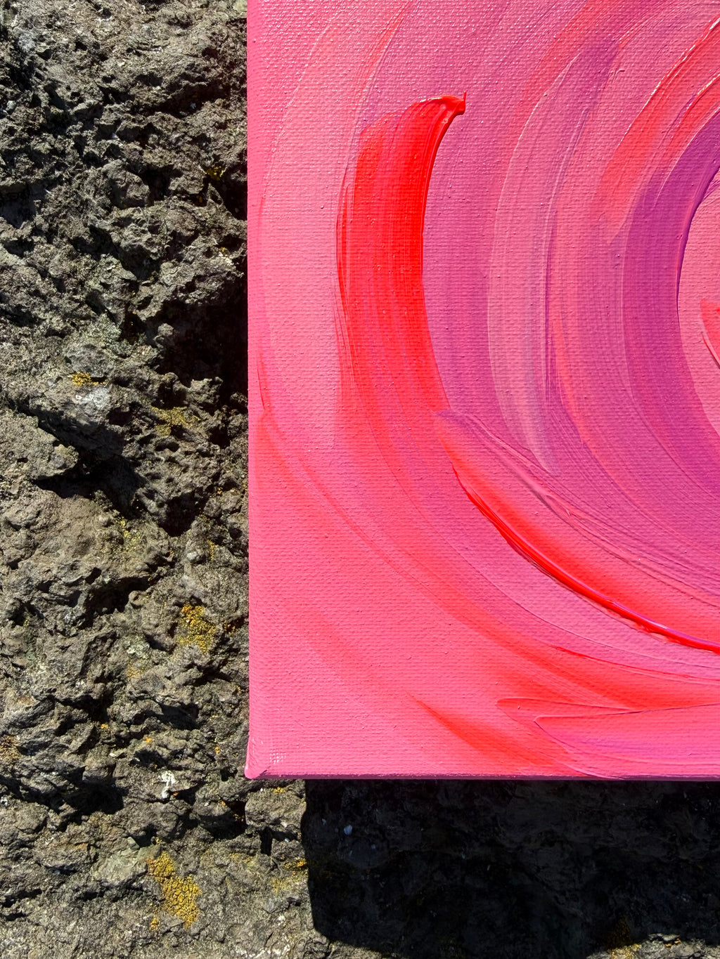 Pink abstract painting leaning against a textured stone wall.