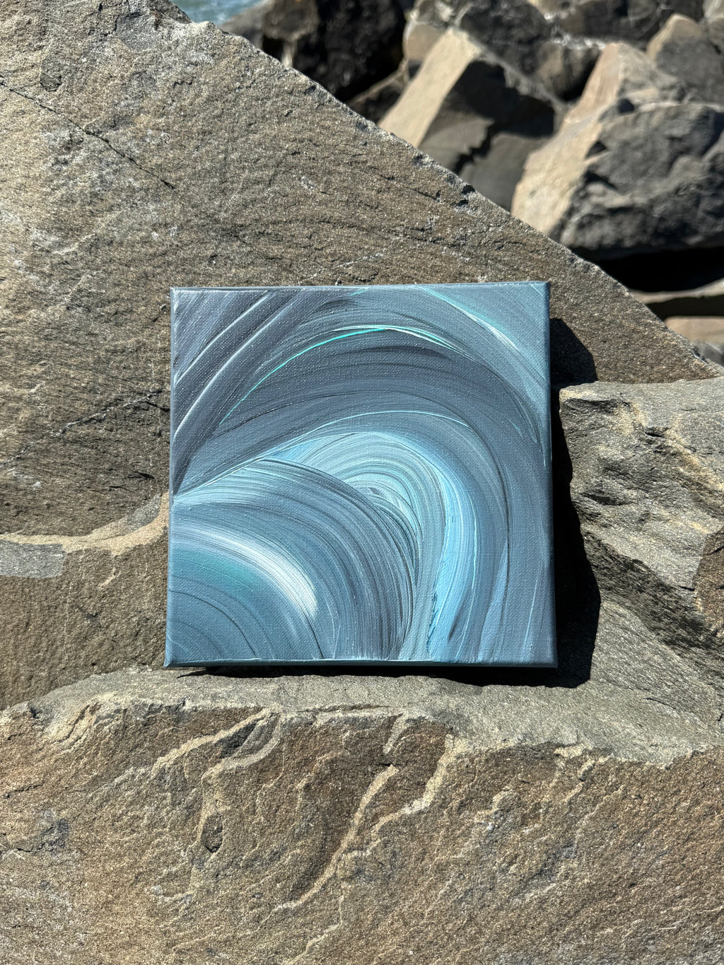 Square piece of abstract art with blue and gray swirls on a rock surface